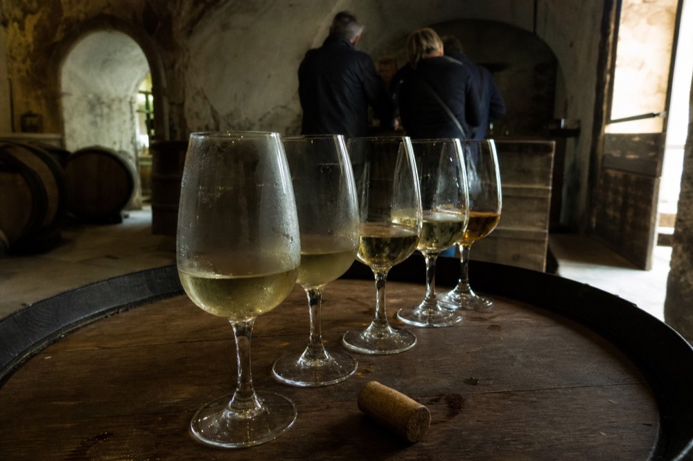 A tasting flight of white wines on a wooden counter in a Soave cellar, no text, no logos, no people
