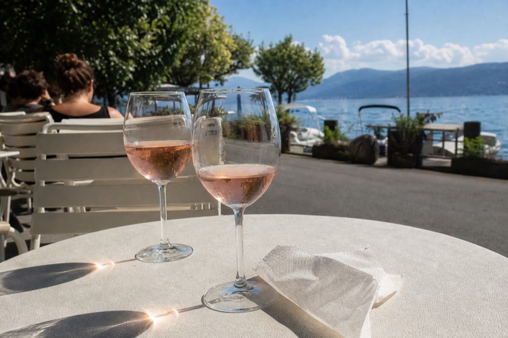 Pale rosé wine in glasses at a lakeside table, no text, no logos, no people