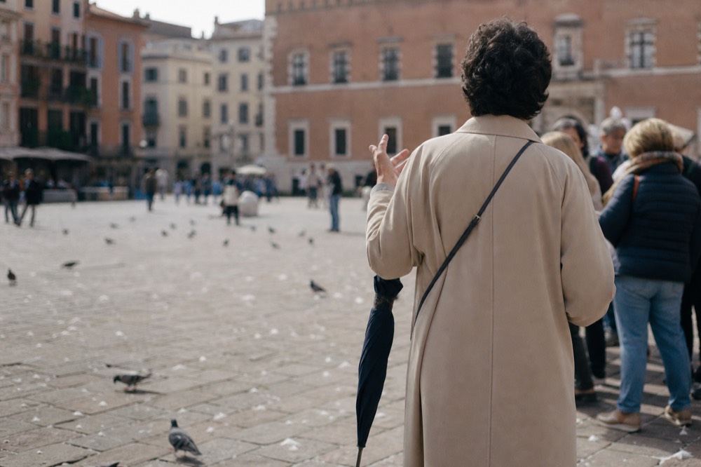 A guide with an umbrella speaking to a small group in a Verona piazza, no text, no logos, no people