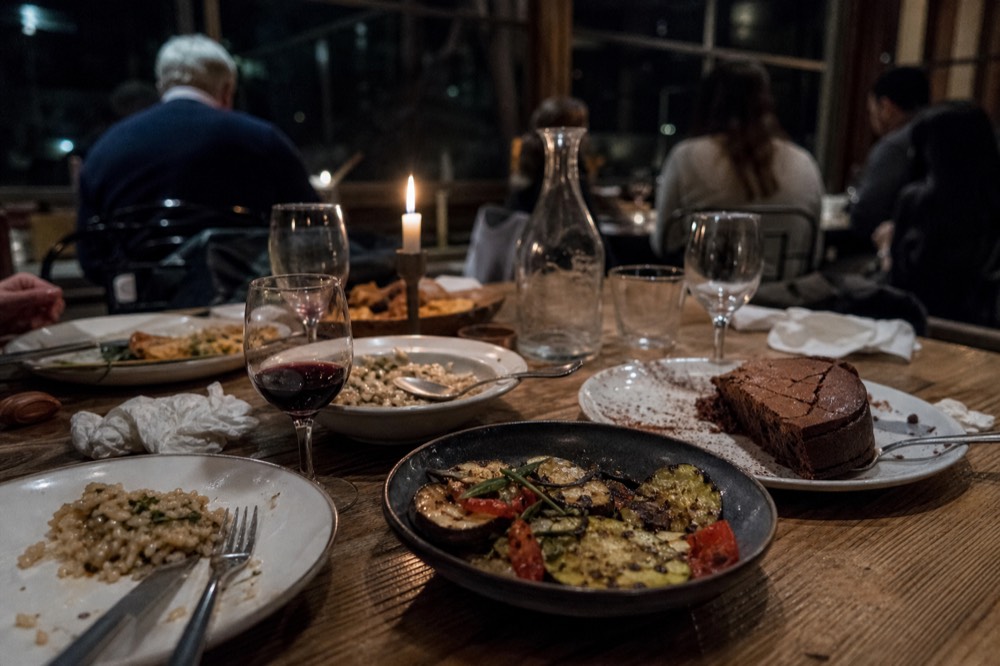 A spread of Veronese dishes on a rustic table: risotto, grilled vegetables, and a chocolate cake, with a glass of red wine, no text, no logos, no people