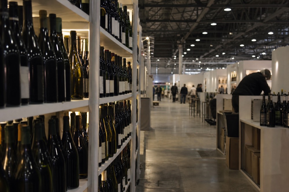 Rows of exhibition stands with wine bottles in a large fair pavilion, no text, no logos, no people