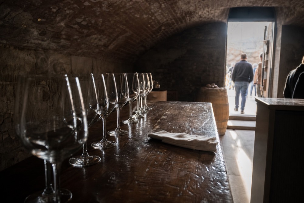 Wine glasses lined up on a wooden counter in a vaulted cellar venue, no text, no logos, no people