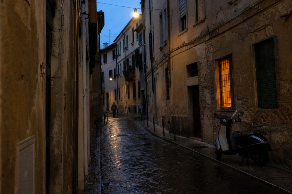 Narrow cobbled street in central Verona at dusk with closed shutters, no text, no logos, no people